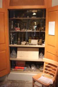 The Below Stairs Lighting Cabinet at Harewood House, featuring candlesticks, oil lamps and electrical fittings.